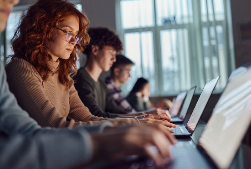 A row of people sitting at desks all working on laptops in front of them.
