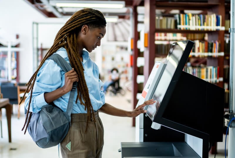 Woman interacting with a touch-screen device in a library.