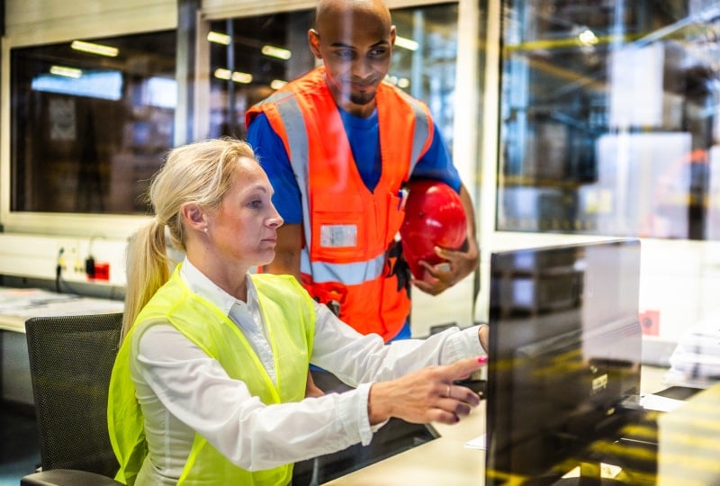 两名员工在生产工厂的办公室内查看显示器上的数据。