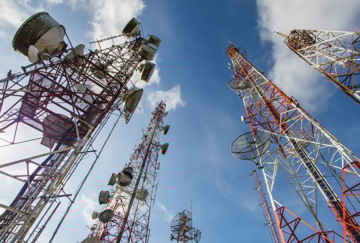 Upward facing shot of multiple network towers beneath a blue sky.
