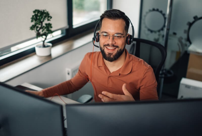 Man talking through a customer support headset and interacting with his desktop computer.