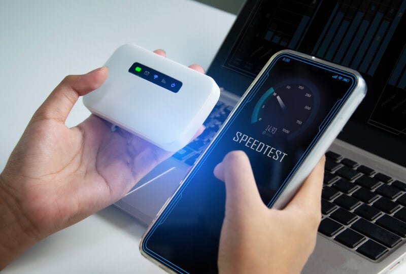 Person holding a smartphone in their right hand and a portable internet router in their left, and conducting a network speed test on the phone.