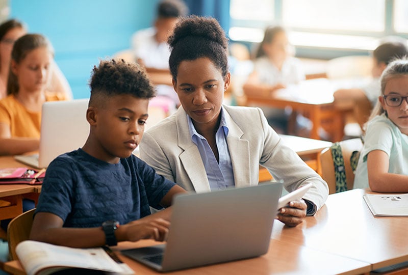 teacher assisting student on laptop at students desk