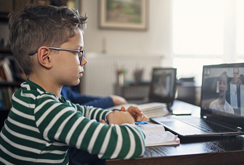young boy in virtual meeting while taking notes