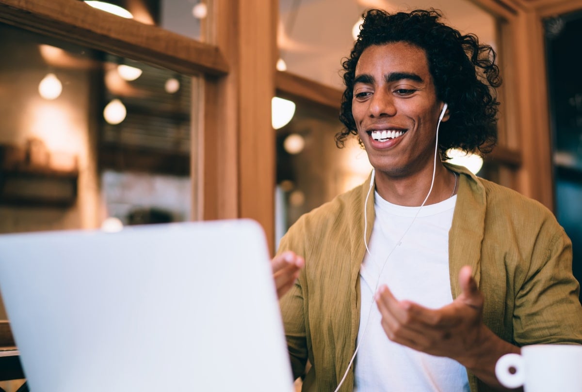 Smiling man wearing wired head phones and gesturing towards a laptop.