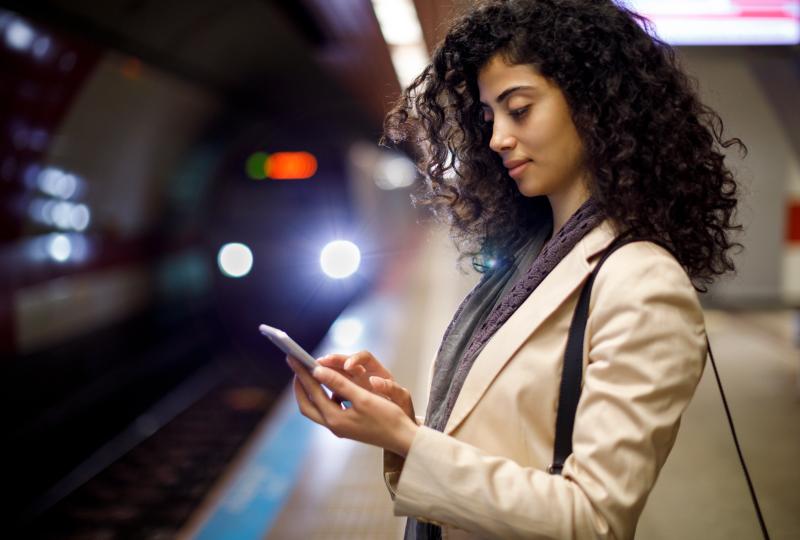 Woman standing near the edge of an underground metro platform interacting with her phone as the train approaches.