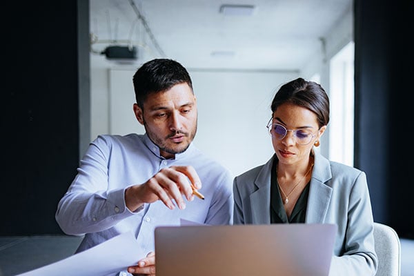 Two professionals look at a laptop together in a bright office