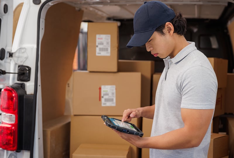 Delivery driver wearing a baseball cap analyzing a mobile tablet device in his hands.