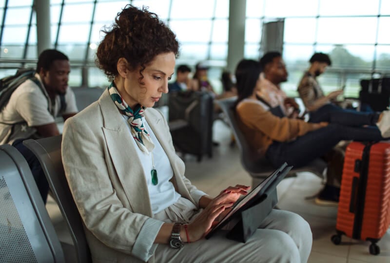 A woman sitting in a airport terminal interacting with a tablet computer.