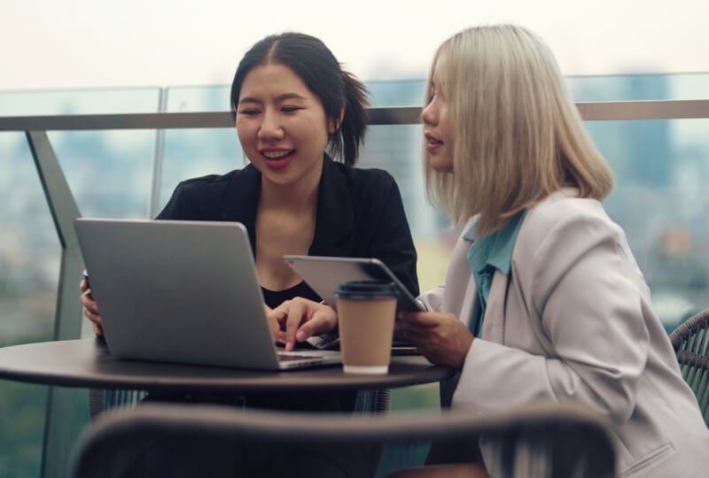 Two women interacting with a laptop and a tablet computer.